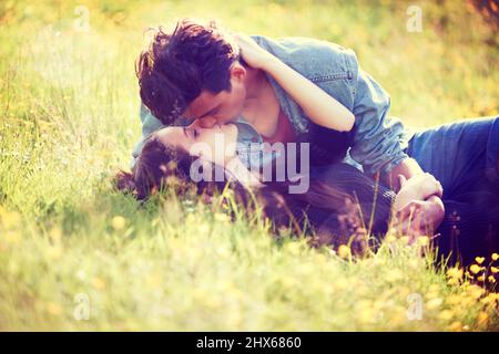 Romanticismo giovanile. Immagine in stile vintage di una giovane coppia che bacia romanticamente in un campo estivo. Foto Stock