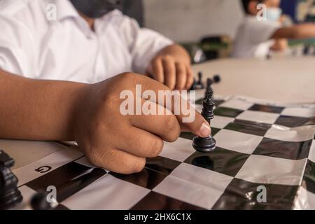 Primo piano della mano di un bambino della scuola muovendo il pezzo del re su una scacchiera Foto Stock