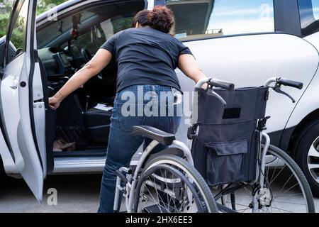 Donna asiatica pieghevole e sollevare la sedia a rotelle nella sua auto. Concetto di accessibilità. Foto Stock