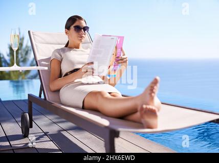 Godendo la sua vacanza. Una giovane donna attraente che legge una rivista mentre si trova su una sedia a sdraio. Foto Stock