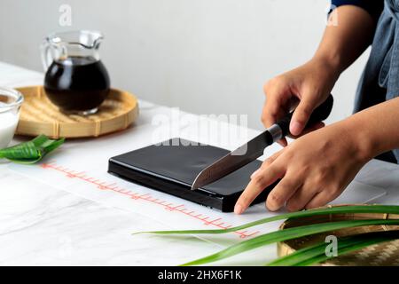 Donna Homemaker taglio Cincau Hitam o Black Grass Jelly Pudding in pezzi, cibo sano Foto Stock