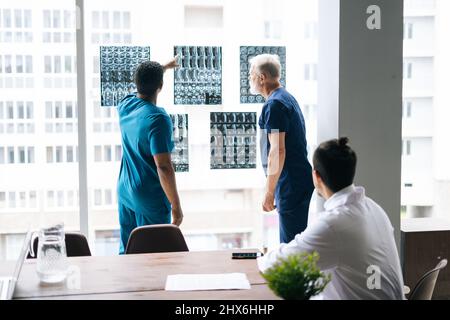 Gruppo di medici esperti multietnici che discutono insieme storia della malattia del paziente utilizzando la scansione MRI durante la conferenza medica in piedi vicino alla finestra. Foto Stock