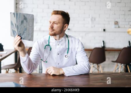 Ritratto di medico maschile concentrato in uniforme bianca esame cervello computerizzato tomografia scansione seduta alla scrivania in ospedale ufficio, Foto Stock