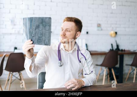 Ritratto di medico maschile messo a fuoco indossando uniforme bianca esame cervello computerizzato tomografia scansione seduta alla scrivania in ospedale ufficio. Foto Stock