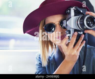 Scattare foto per tutta la vita. Una giovane donna che indossa un cappello e occhiali da sole scattando foto da un'auto. Foto Stock