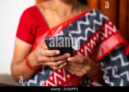 Primo piano di una donna indiana impegnata a utilizzare il telefono cellulare a casa - concetto di tecnologia, utilizzando i social media, internet e relax. Foto Stock