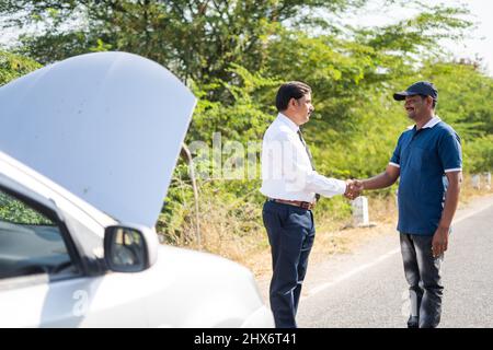 Saluto uomo d'affari scuotendo le mani con meccanico auto per la riparazione di auto rotta su autostrada - concetto di servizio di riparazione auto mobile e supporto da Foto Stock