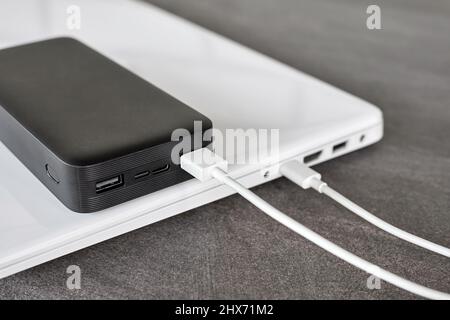 Power Bank ricarica un computer portatile tramite cavo USB di tipo C su sfondo grigio in pietra Foto Stock