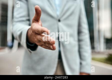 Permettiamo di rendere questa città migliore insieme. Primo piano di un uomo d'affari irriconoscibile che estende una stretta di mano in città. Foto Stock