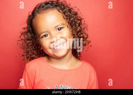 Una bambina marrone con capelli marroni, ricci ben definiti che si aggirano per esprimere espressioni e messaggi attraverso i suoi occhi, il suo viso e i suoi subli Foto Stock