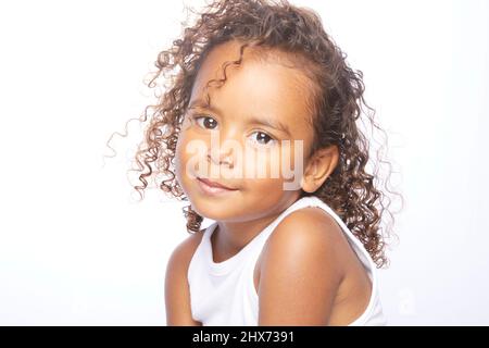 Una bambina marrone con capelli marroni, ricci ben definiti che si aggirano per esprimere espressioni e messaggi attraverso i suoi occhi, il suo viso e i suoi subli Foto Stock