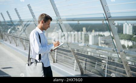 giovane uomo con una borsa per computer portatile che fa appunti in un notebook . Foto Stock