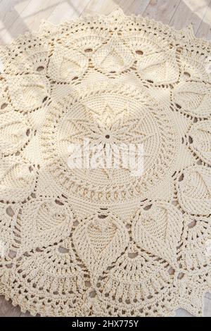 Tappeto lavorato a maglia fatto in casa di fili spessi, fatto a mano: Un tappeto fatto a mano di fili beige giace sul pavimento, il sole splende su di esso Foto Stock
