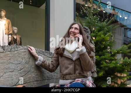 Giovane donna felice seduta su una panca e parlare al telefono in inverno Foto Stock