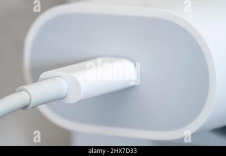 Primo piano macro di un caricabatterie per telefono cellulare collegato a una parete con un cavo Foto Stock