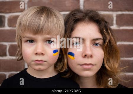 facce di ragazzo e giovane donna con bandiera blu e gialla dipinta sulle guance. Famiglia, unità, sostegno. Gli ucraini sono contrari alla guerra e chiedono aiuto Foto Stock