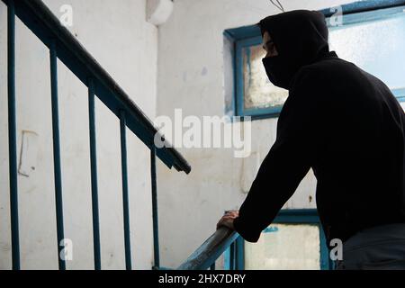 un maniaco, un uomo in un cappuccio nero sta inseguendo qualcuno, salendo le scale. Foto Stock