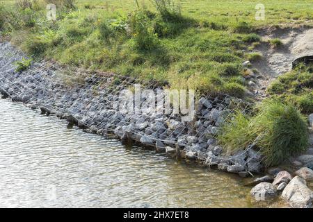 Rafforzare le rive del fiume, rete e pietre. Paesaggio riva del fiume e grandi pietre con rete metallica Foto Stock