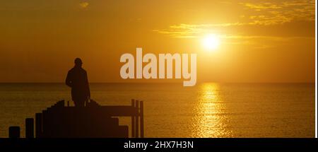 Una vista panoramica di una silhouette uomo che guarda ad un tramonto sereno sull'oceano Foto Stock
