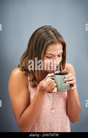 Il caffè fresco puzza Studio girato di una giovane donna che beve una tazza di caffè su uno sfondo grigio. Foto Stock