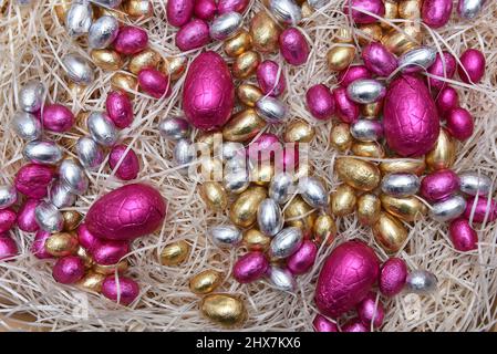 Mucchio di colori pastello pallido foglio avvolto cioccolato pasqua uova in rosa, argento e oro, su nido crema pallido. Foto Stock