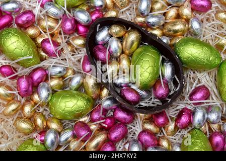 Mucchio di coloratissimi fogli di cioccolato uova di pasqua in verde, rosa, giallo e oro con metà di un grande uovo di cioccolato marrone scuro. Foto Stock