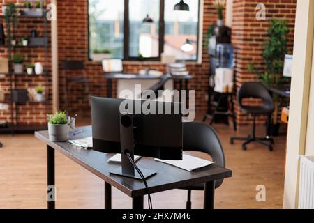 Interno di un ufficio aziendale vuoto con mobili e nessuno in esso. Moderno spazio di lavoro dell'agenzia di marketing aziendale con scrivanie e computer desktop contemporanei che mostrano grafici finanziari. Foto Stock