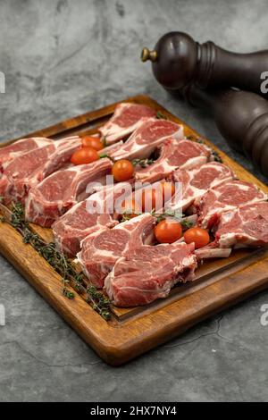 Costolette di agnello su sfondo scuro. Costolette di agnello crudo su tavola di servizio in legno Foto Stock