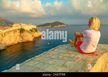 Donna che riposa sulla fortezza di Lovrijenac sopra il Porto Ovest. Skyline di Dubrovnik con Fort Bokar in Croazia. Storica città murata in Dalmazia e. Foto Stock