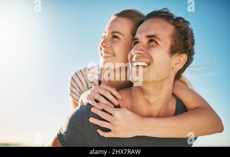 Sono qui giorni più luminosi e giorni migliori. Scatto di una giovane coppia felice godendo un giro di piggyback all'aperto. Foto Stock