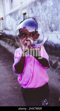 Un bambino piccolo gioca con un pallone gonfiabile durante il giorno nel mezzo della strada in un villaggio nella città di Ambon, il villaggio è chiamato Hatalai Foto Stock