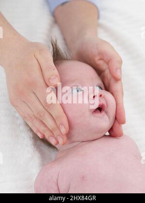 Tenere la testa della bambina delicatamente tra le mani per il massaggio, 6 settimane Foto Stock