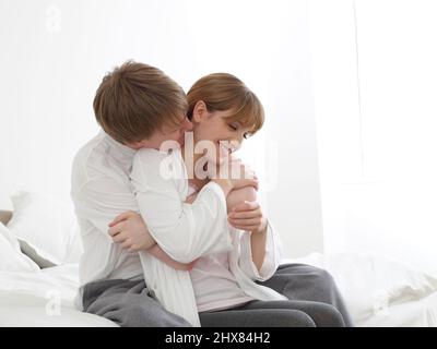 Donna seduta sul letto accanto ad un uomo, coccolante Foto Stock