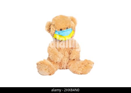 L'orso di Teddy indossa PP non tessuto maschera medica monouso tonica in giallo e blu di bandiera Ucraina isolato su sfondo bianco. Foto Stock