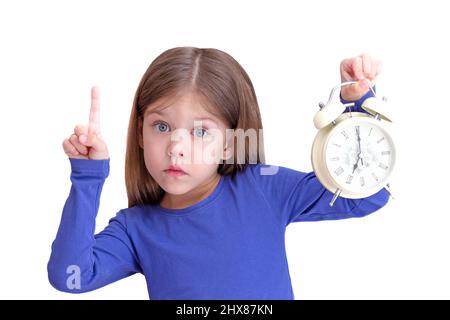 Allarme bambino con orologio alle 7:00, concetto di svegliarsi presto e tenere in mano l'indice, isolato su sfondo bianco guardando la fotocamera Foto Stock