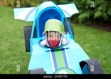 Bambini che indossano modelli di auto da corsa in cartone/costume, giocando in giardino Foto Stock