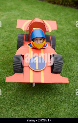Bambini che indossano modelli di auto da corsa in cartone/costume, giocando in giardino Foto Stock
