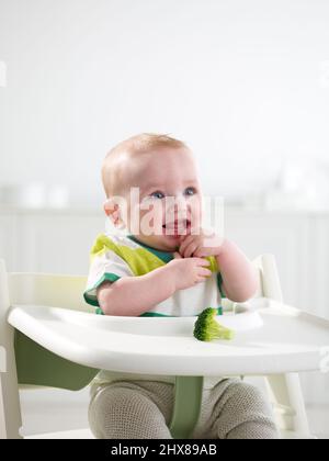 Bambino di 6 mesi che mangia in seggiolone Foto Stock