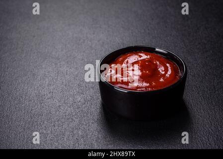 Ketchup in una pentola di ceramica. Sfondo in cemento nero Foto Stock