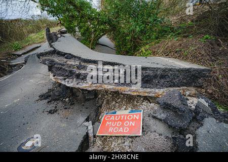 Un cartello che indica il fango sulla strada si trova su una sezione gravemente danneggiata del B4069 vicino a Lyneham nel Wiltshire, che è ancora in movimento e cambia forma, a seguito di uno scivolamento di terra nel mese di febbraio. Data foto: Giovedì 10 marzo 2022. Foto Stock