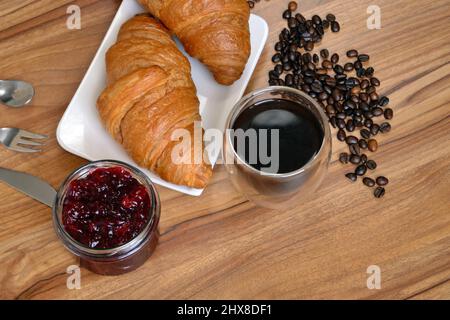 Croissant appena sfornati a colazione con una tazza di caffè e un vasetto di marmellata di frutti di bosco Foto Stock