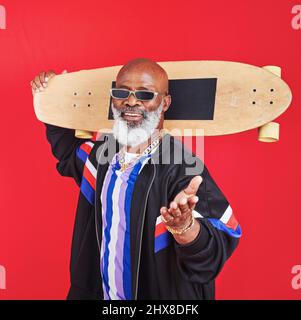 Il mio skateboard mi rende ancora più fresco. Scatto di un uomo maturo che tiene uno skateboard su sfondo rosso. Foto Stock