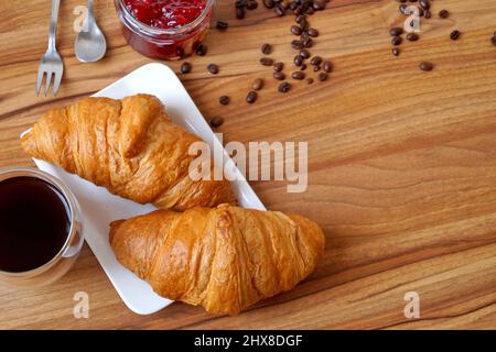 Su un piatto rettangolare bianco ci sono due croissant per la colazione. Nelle vicinanze troverete anche marmellate e caffè. Foto Stock
