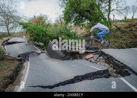 Un uomo su una BMX salta sopra un gap nel asfalto rotto su una sezione del B4069 vicino Lyneham nel Wiltshire, che è ancora in movimento e in cambiamento di forma, a seguito di una striscia di terra nel mese di febbraio. Data foto: Giovedì 10 marzo 2022. Foto Stock