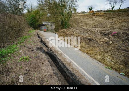 Il fango copre la maggior parte della carreggiata e grandi lacune appaiono su una sezione del B4069 vicino a Lyneham nel Wiltshire, che è ancora in movimento e cambia forma, a seguito di una striscia di terra nel mese di febbraio. Data foto: Giovedì 10 marzo 2022. Foto Stock