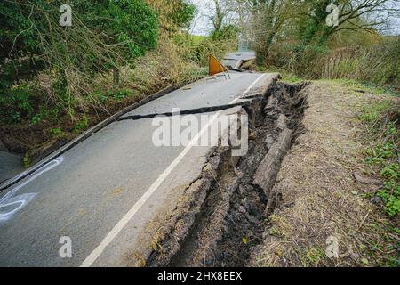 Alberi e cedimenti inghiottiscono una metà della strada carrozza e grandi lacune appaiono su una sezione del B4069 vicino a Lyneham nel Wiltshire, che è ancora in movimento e cambia forma, a seguito di una striscia di terra nel mese di febbraio. Data foto: Giovedì 10 marzo 2022. Foto Stock