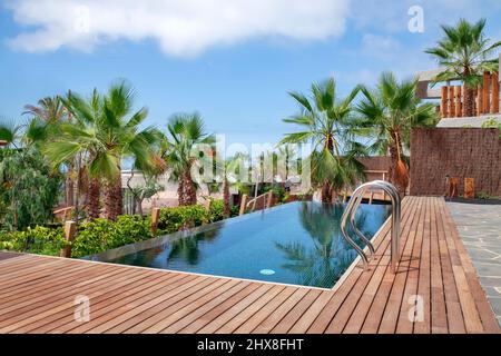 Lussuosa piscina con acqua blu chiara e circondata da palme tropicali e terrazze di sequoie, parte di una proprietà residenziale, il resort Abama Foto Stock