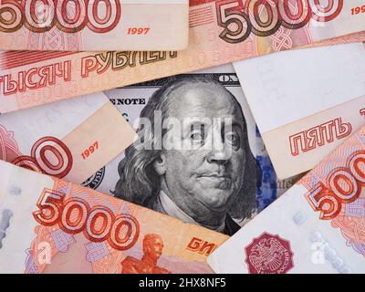 Un conto di cento dollari sotto circa cinquemila banconote rubli. Primo piano. Foto Stock