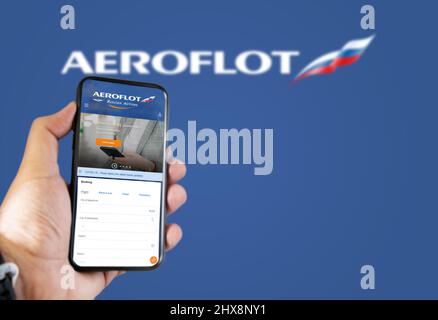 Mosca, Gennaio 2022: Tenere un telefono con Aeroflot russo compagnie aeree richiesta di prenotazione voli. Logo Aeroflot sfocato su sfondo blu. Prenota Foto Stock