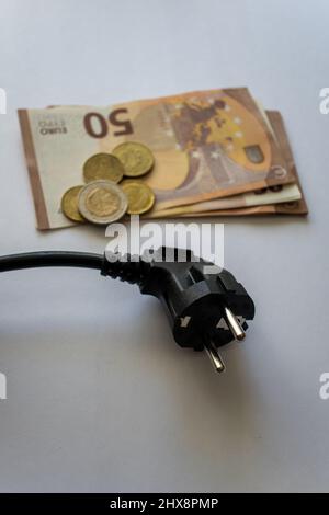 Presa di corrente nera sulle banconote in euro su una superficie bianca in legno. Energia costosa e costo di concetti di elettricità. Vista dall'alto. Foto Stock